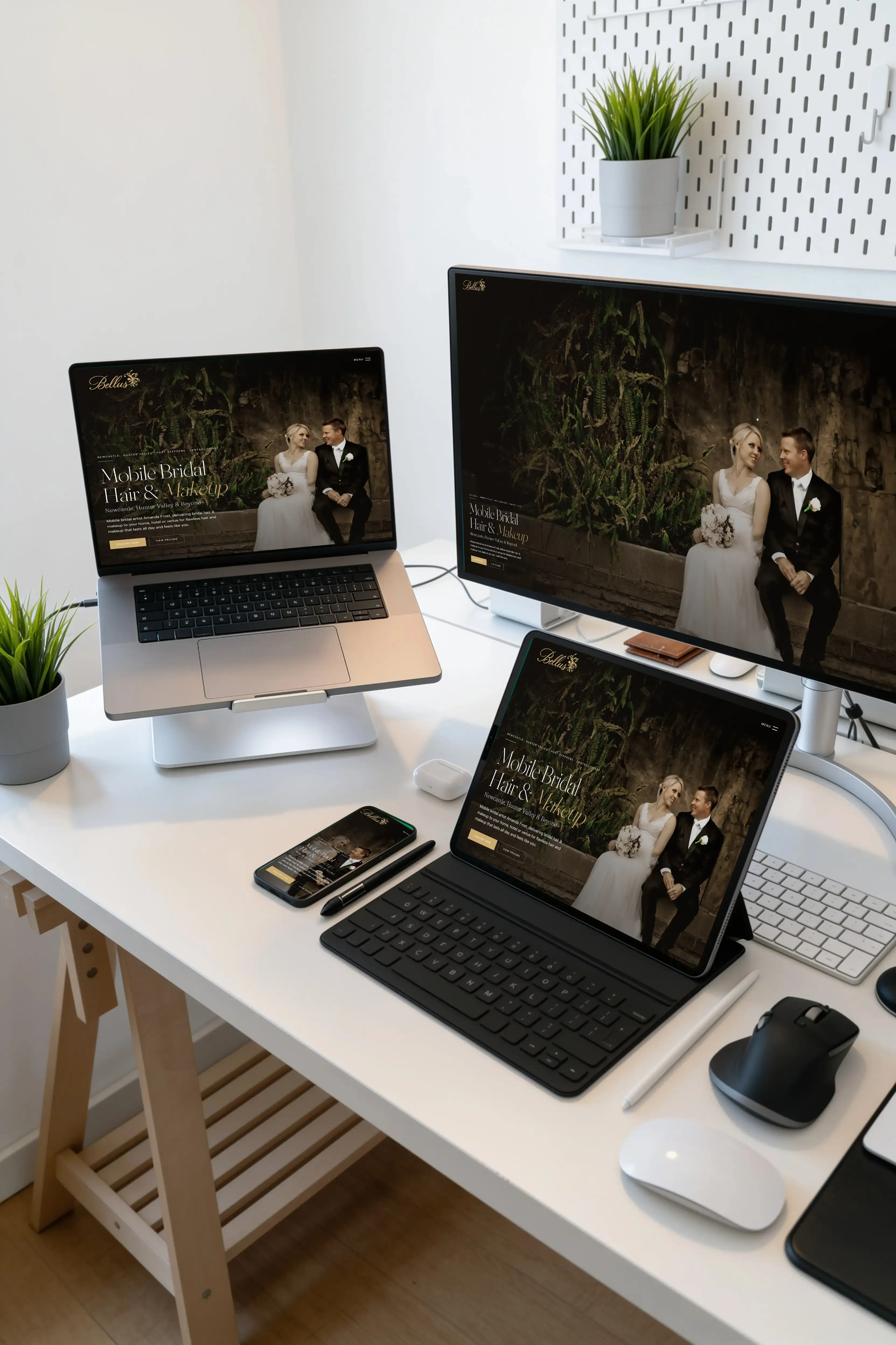 The Bellus home page running at once on a laptop, a widescreen monitor, a tablet on a keyboard case and a phone, laid out on a white studio desk.