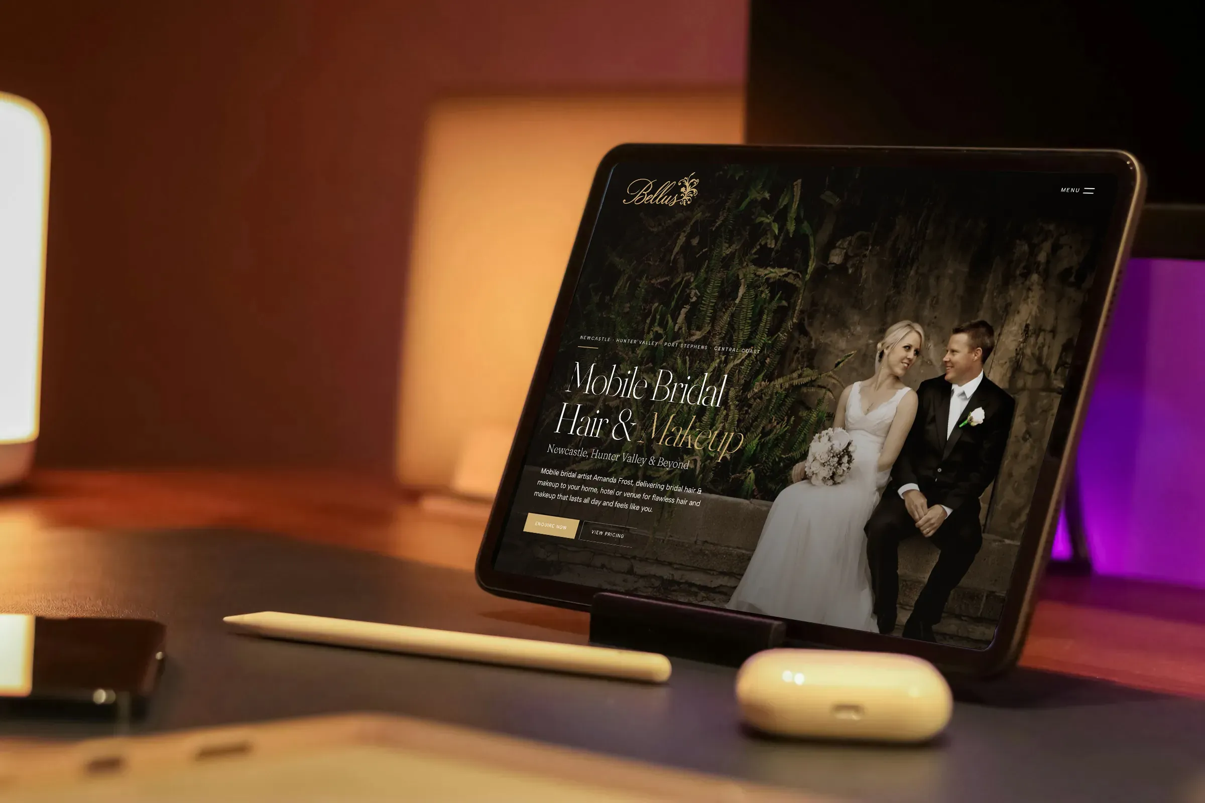The Bellus home page on a tablet propped on a warmly lit desk, beside a stylus and a pair of earbuds.