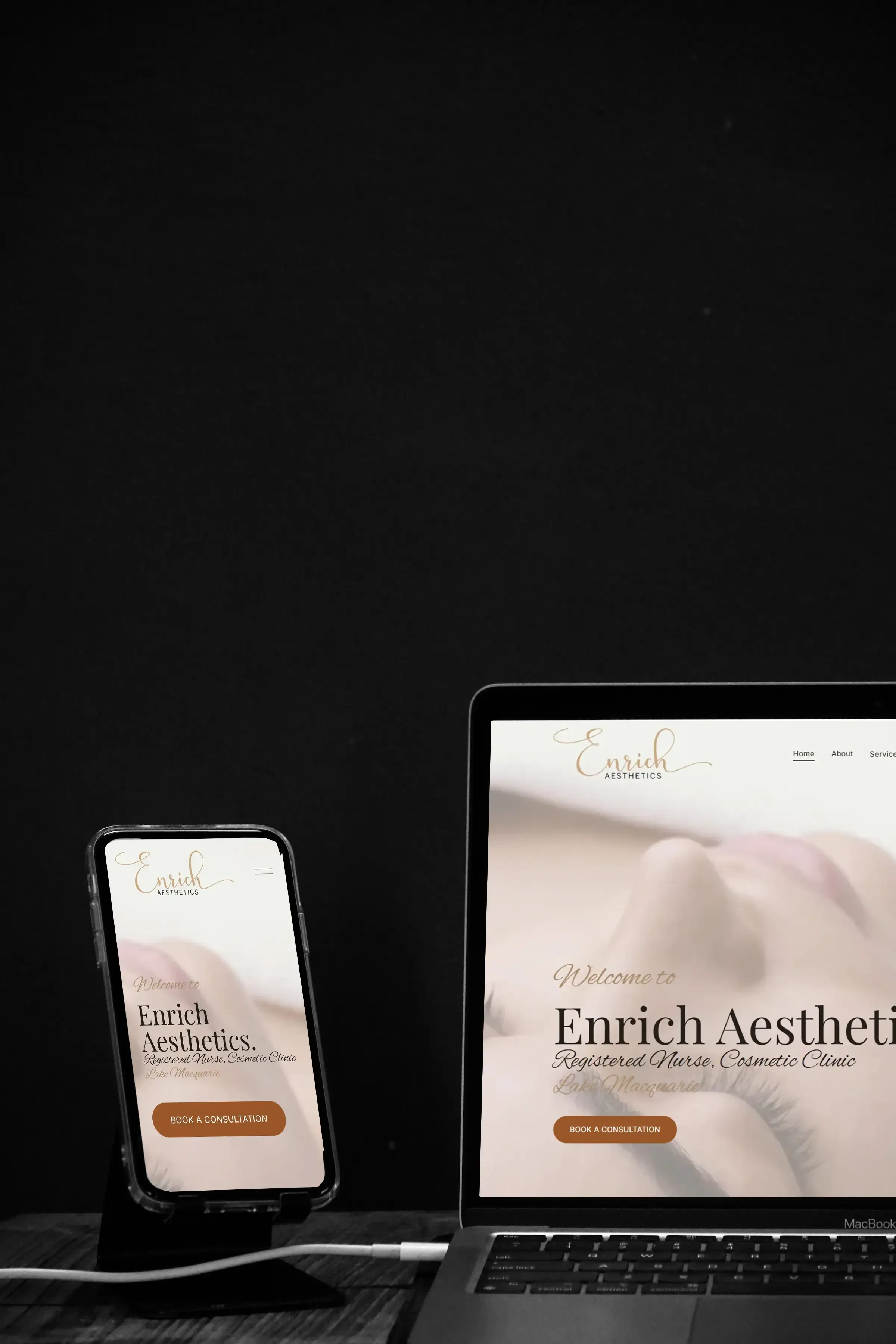 The Enrich Aesthetics home page running on a phone and a laptop side by side on a dark desk.